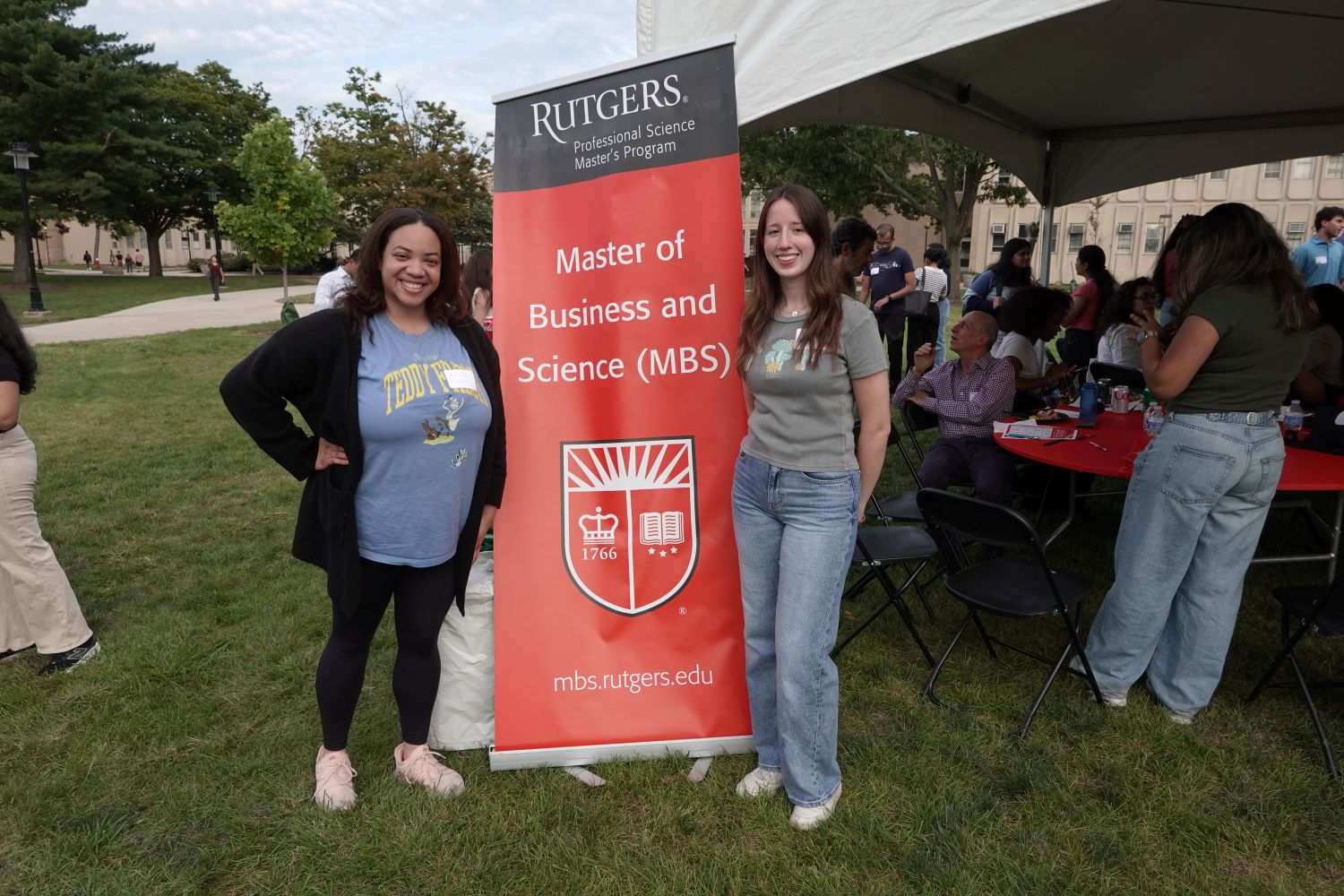 Two students posing with the event banner