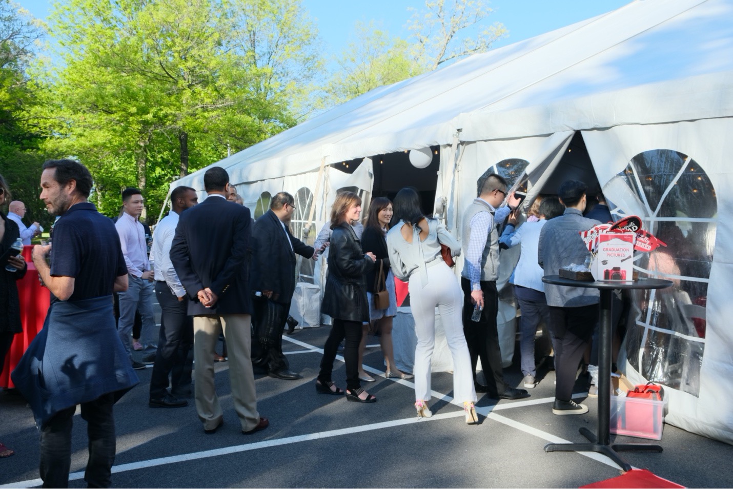 crowd of graduate students mingling outside white canopied tent under blue skies