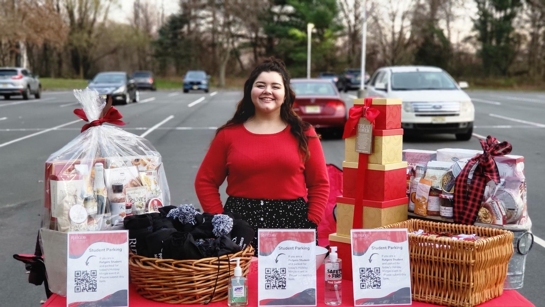 woman in red top and black skirt standing behind table of raffle baskets and gifts
