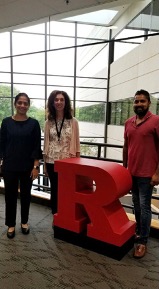 three people standing around a red sculpture of Rutgers University's signature "Block R"