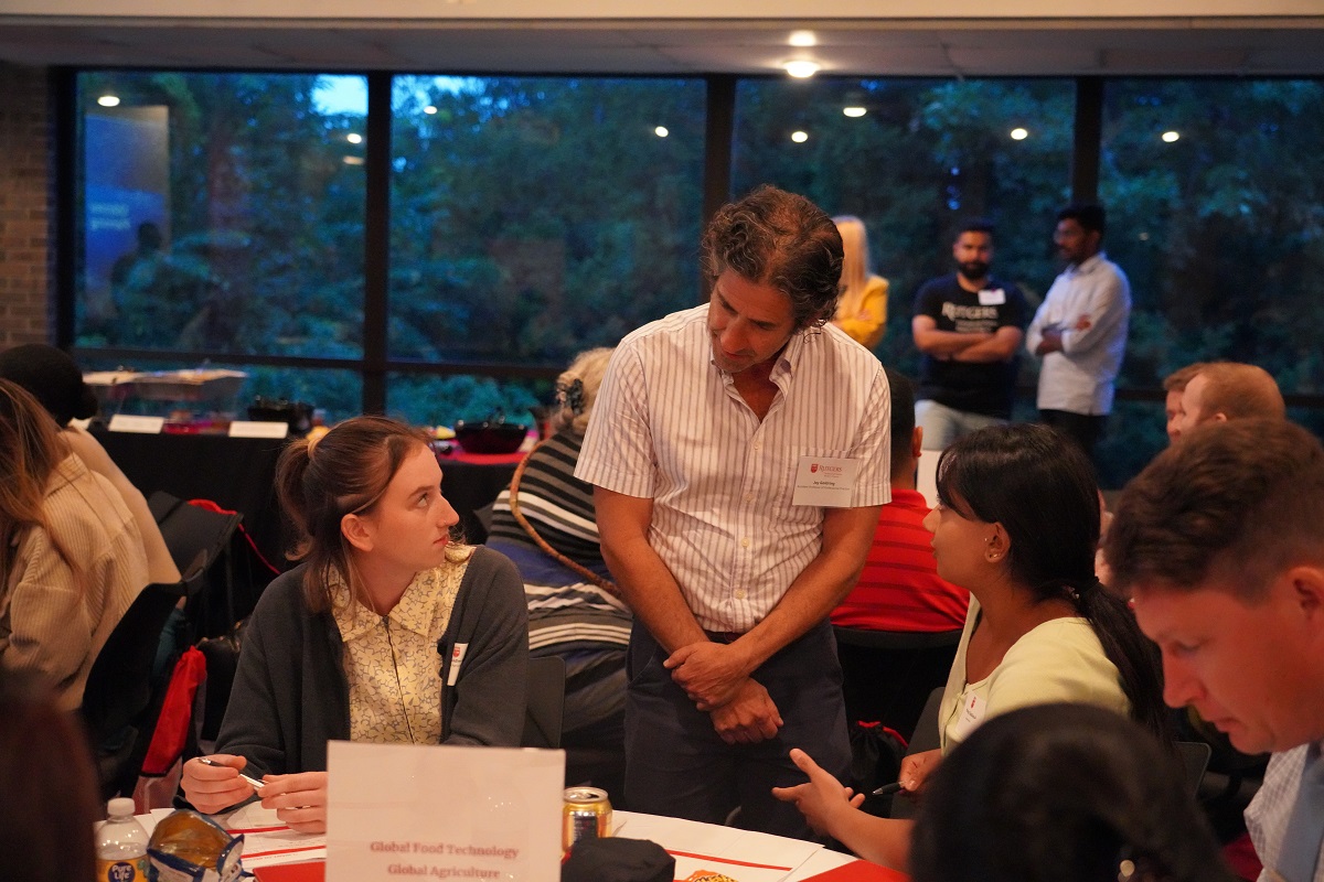 faculty member talking to students sitting at a table.