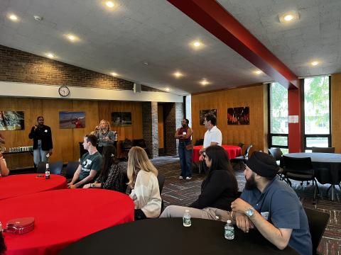 People sitting at tables, looking at woman with microphone